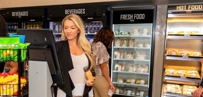 Shoppers choosing from a fresh food cooler and beverage cooler in a workplace market