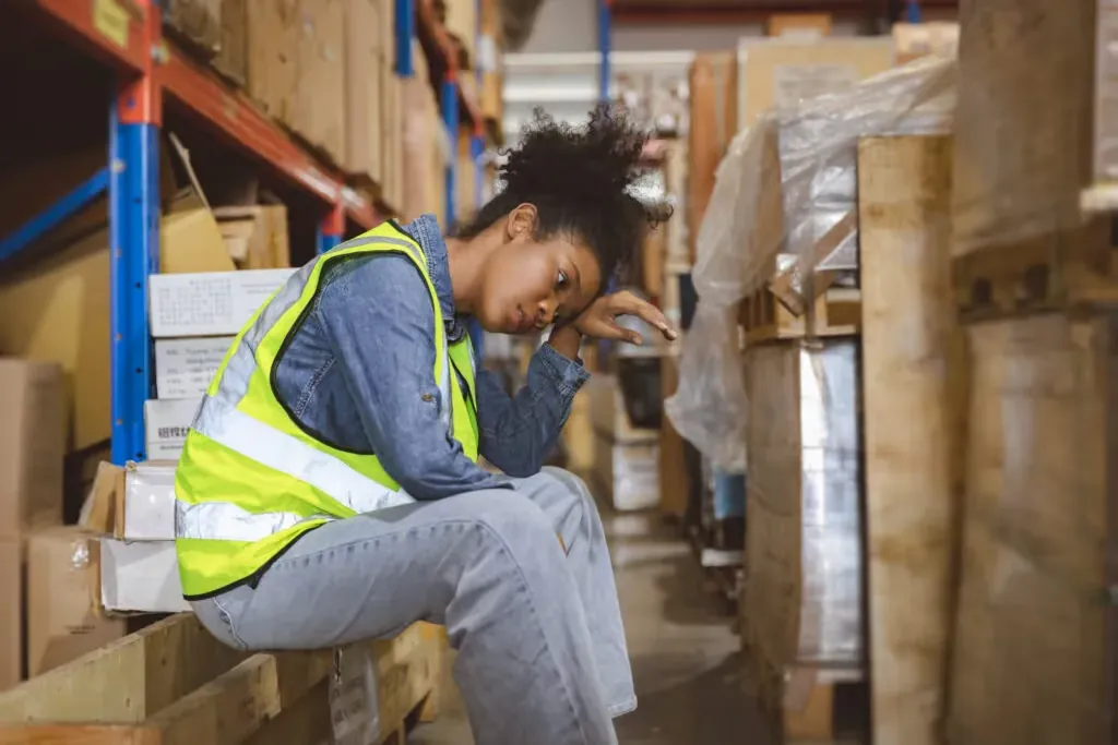 Warehouse worker in a safety vest resting between shelves of boxes