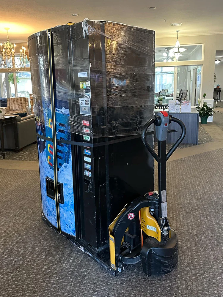 Black vending machine on pallet jack wrapped for safe moving in Dallas Fort Worth