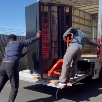 Two movers using a pallet jack to load a vending machine into a truck Texas Vending Moving Dallas Fort Worth