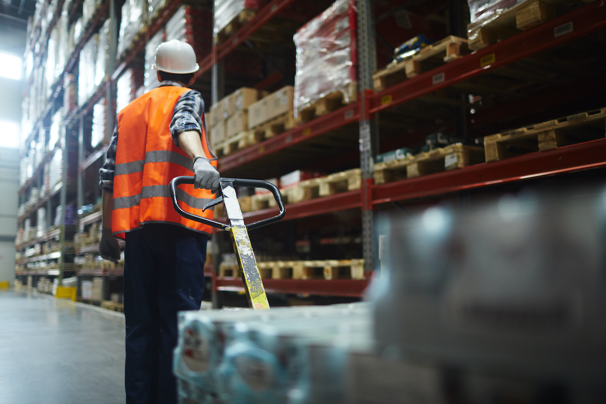 Warehouse worker pulling machine while walking along shelves